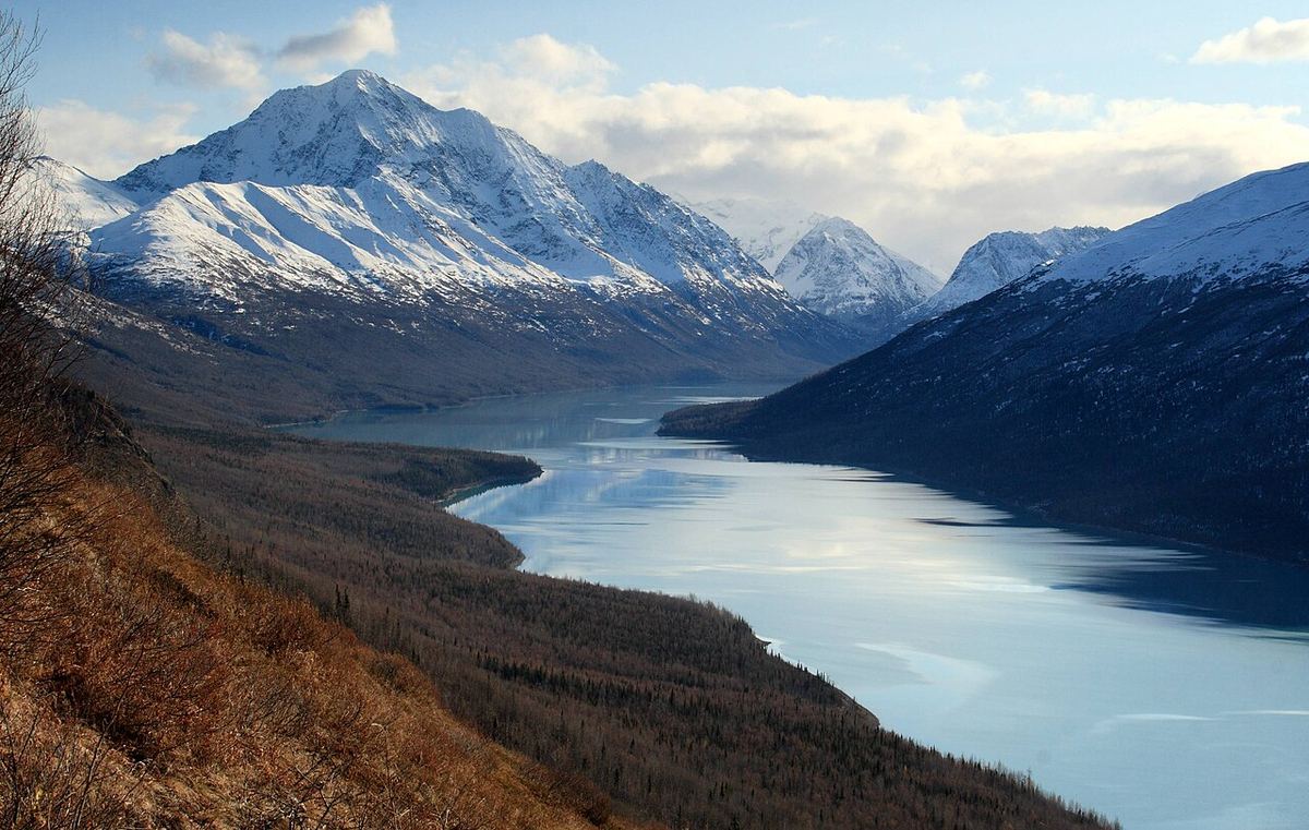 Snow-covered peaks above a long, partly frozen Eklutna Lake, seen from a brown autumn hillside