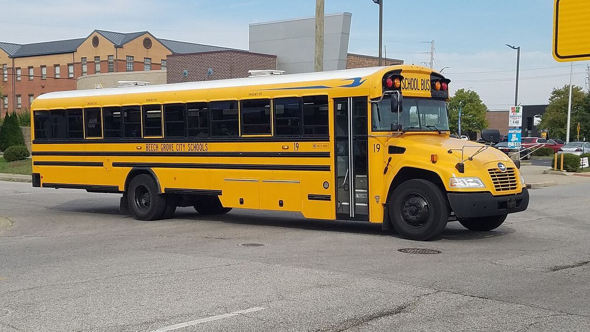 A yellow Blue Bird Vision school bus parked in front of a brick school building