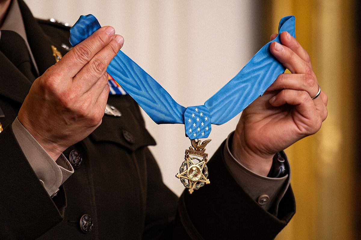 Hands holding up the Army Medal of Honor on its light blue star-spangled ribbon