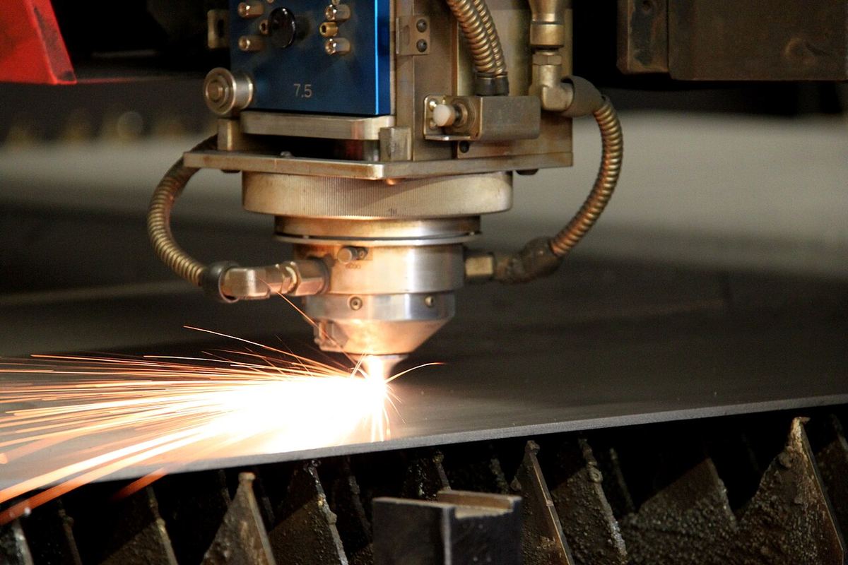 Close-up of an industrial laser head throwing bright sparks as it cuts a sheet of metal