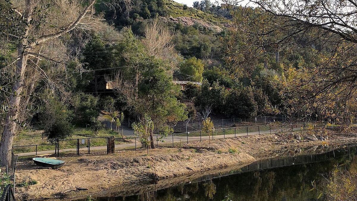 A walking path beside a small lake below green, tree-covered hills in Fallbrook, California